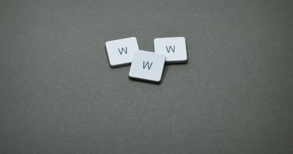 Three white letter tiles, each displaying a black uppercase W casually arranged on a dark gray surface.